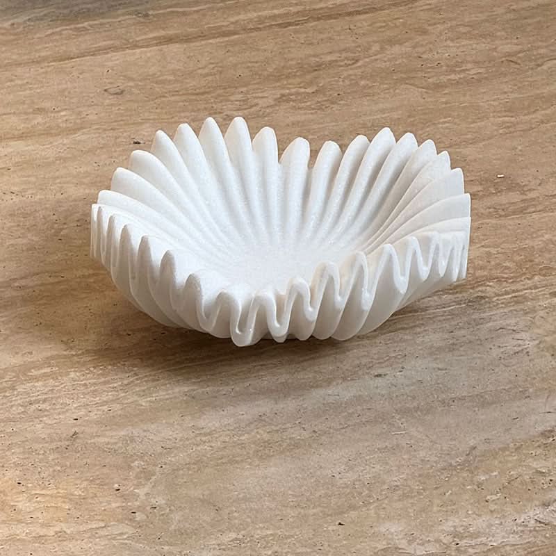 White fluted marble fruit bowl on a textured beige surface.